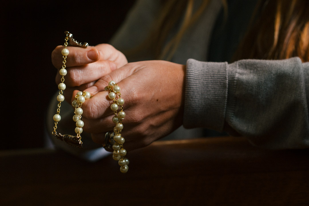 A woman kneels in a pew and prays the rosary